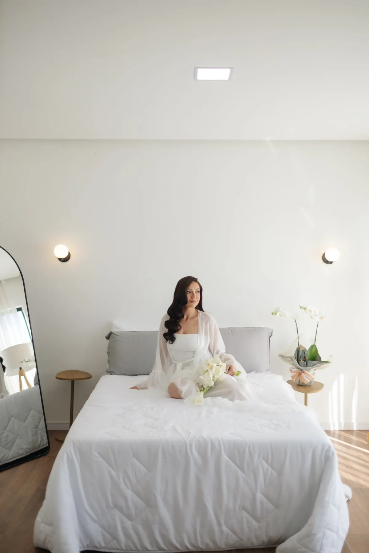 Noiva sentada na cama da suíte master, com luz natural